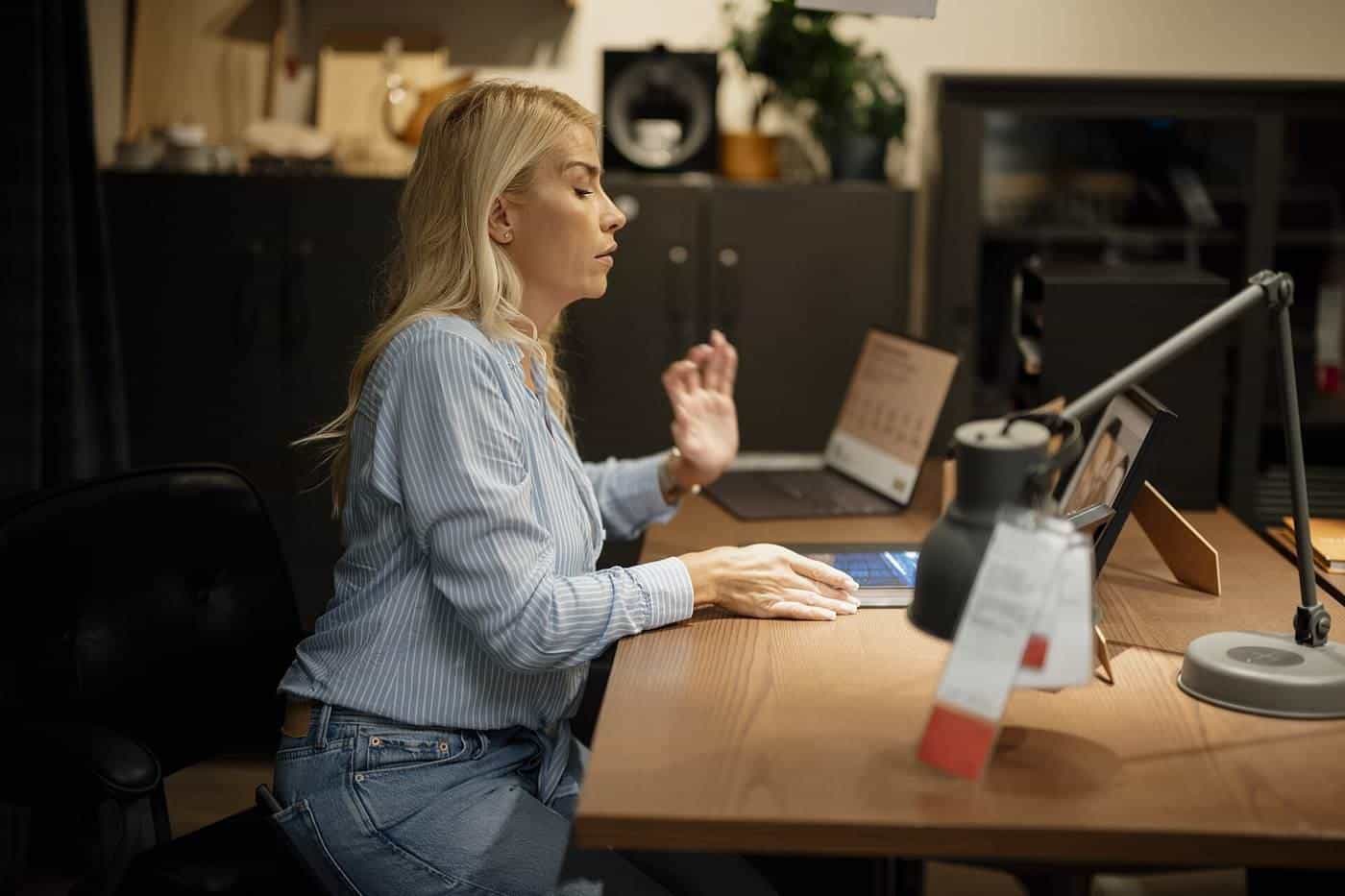 A woman working at a laptop at a wooden desk in a home office