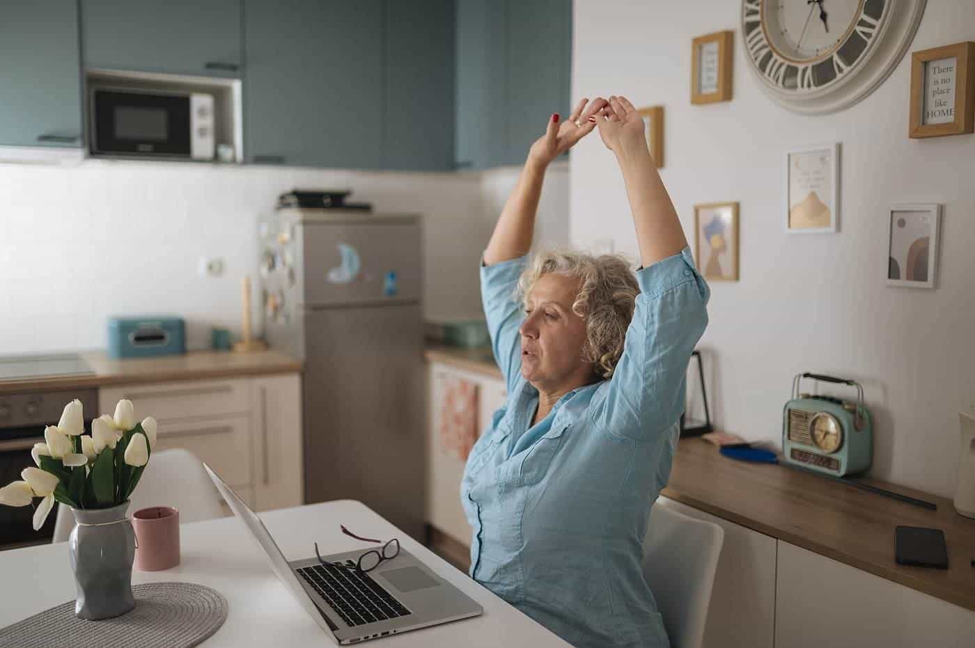 A woman stretching her arms above her head at a home office desk