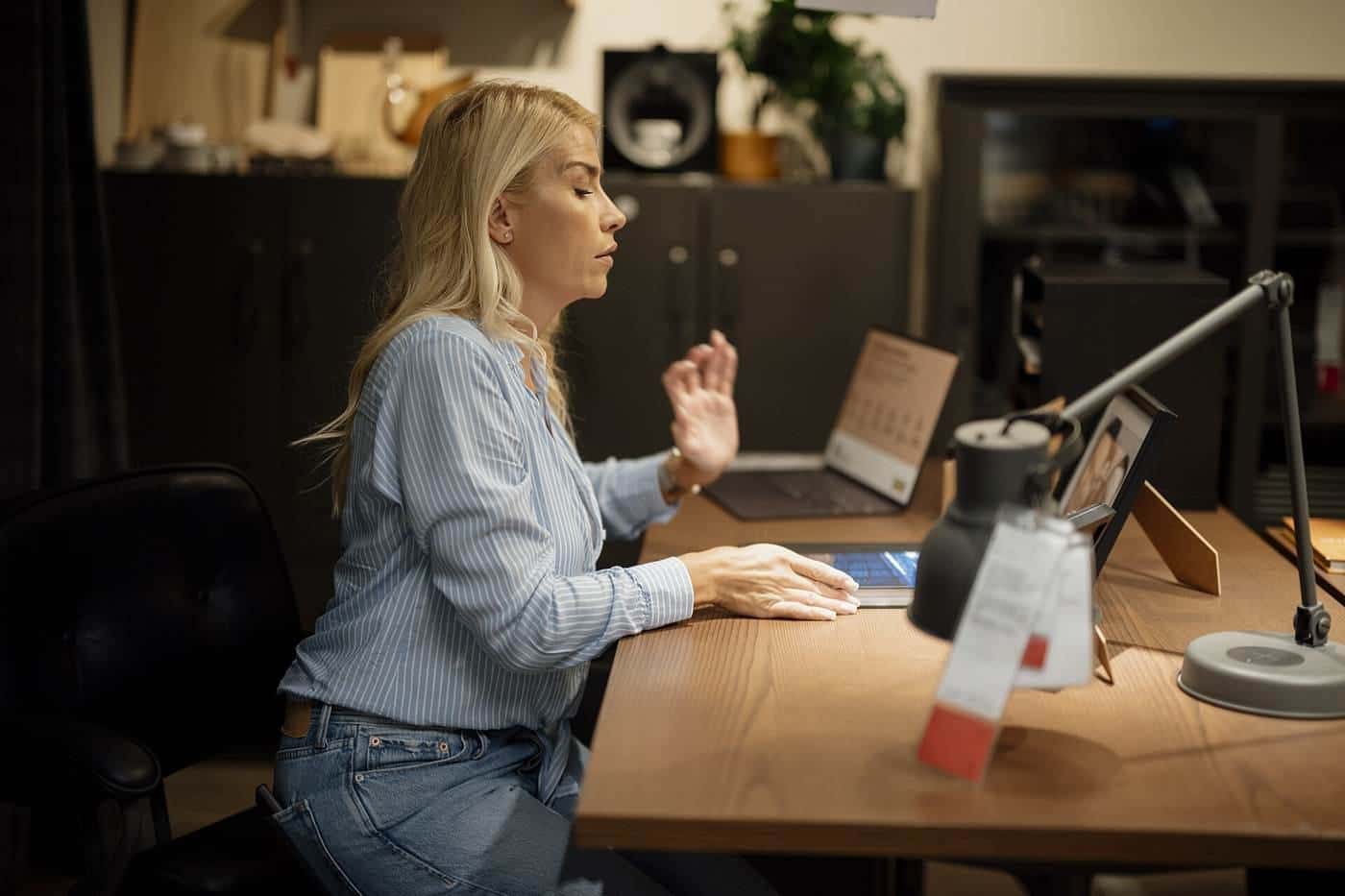 A woman working at a laptop on a wooden desk in a home office