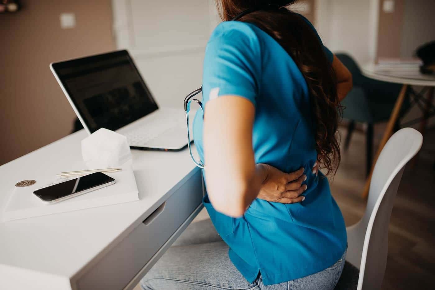 A woman holding her lower back while standing at a home office table