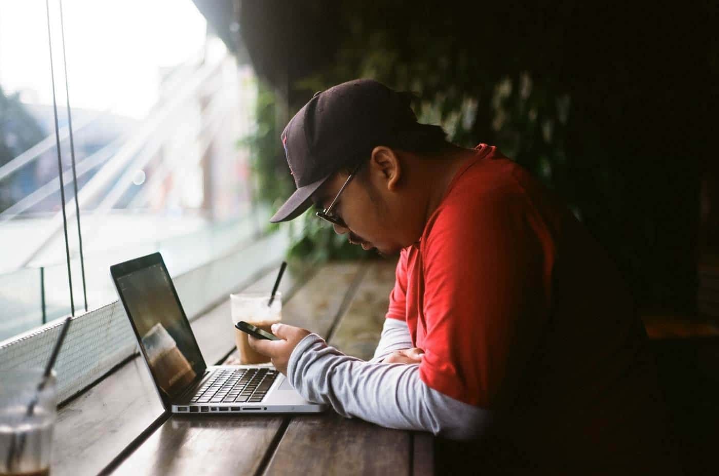 A man in a cap using a laptop at a table by a window