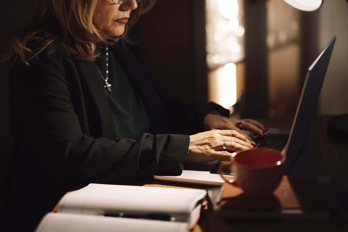 A woman typing on a laptop at a desk with a notebook